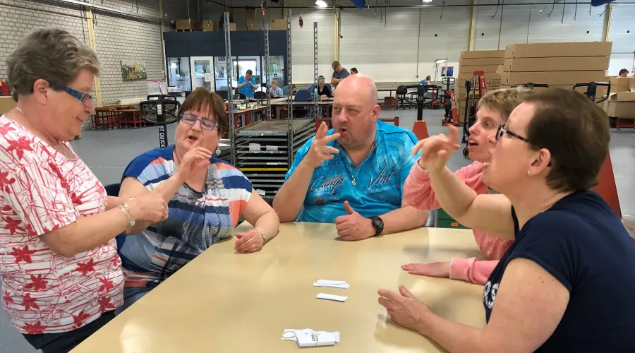 Groep collega's spreekt in gebarentaal met elkaar, zittend aan een tafel