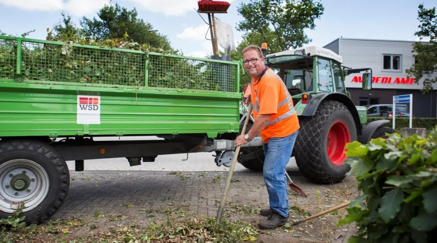 Medewerker ruimt groen op na het snoeien en lacht in de camera