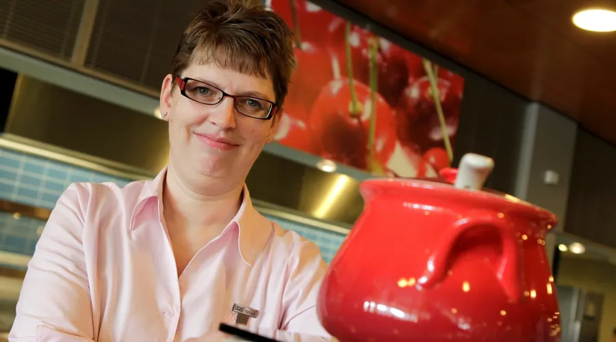 Irma werkt bij Hutten. Ze kijkt in de camera en op de voorgrond is een kop soep te zien
