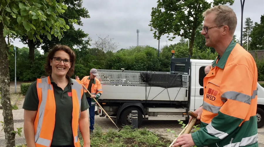 Collega's aan het werk in het groen waarbij een vrouw lachend de camera in kijkt