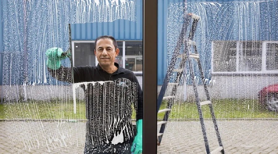 Man wast raam en kijkt lachend in de camera