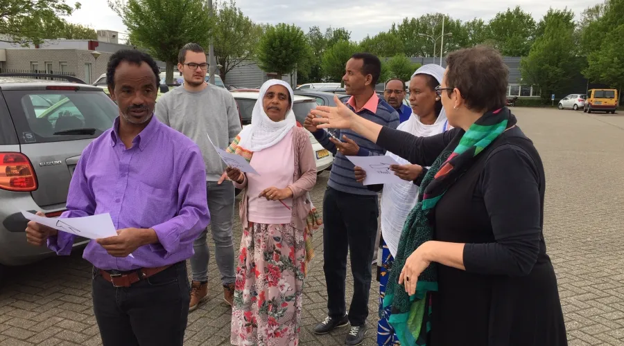 Docent geeft les aan een groepje inburgeraars buiten op een parkeerplaats