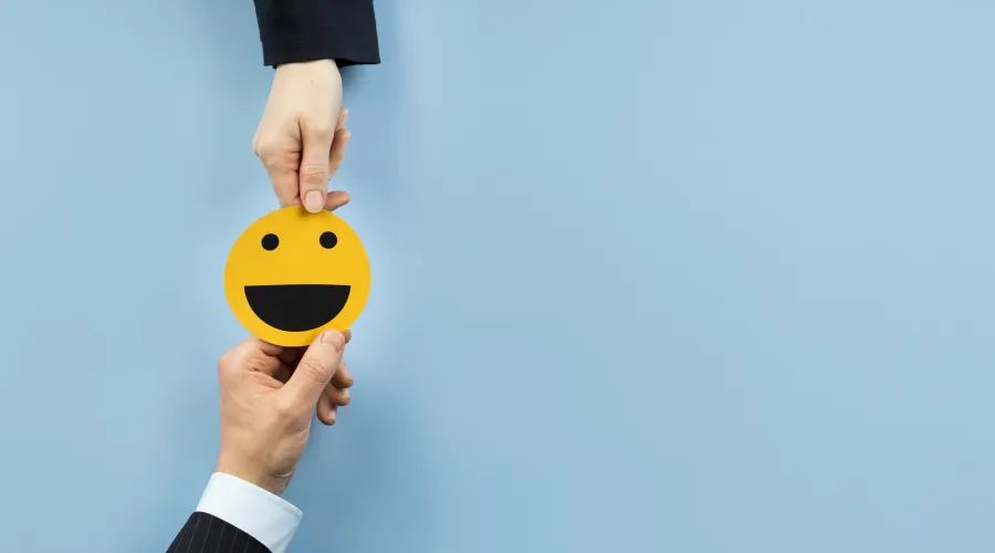 Twee handen die samen een gele smiley vasthouden