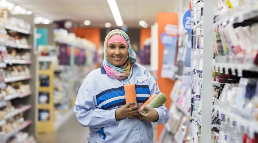 Halima staat in een gangpad bij de Albert Heijn met een aantal producten in haar hand, ze kijkt richting de camera.