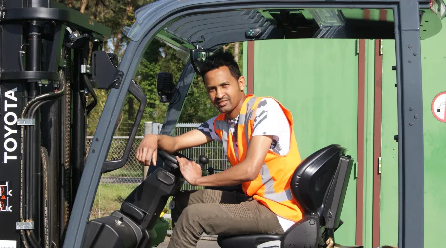 Jonge man zit op een heftruck en kijkt de camera in