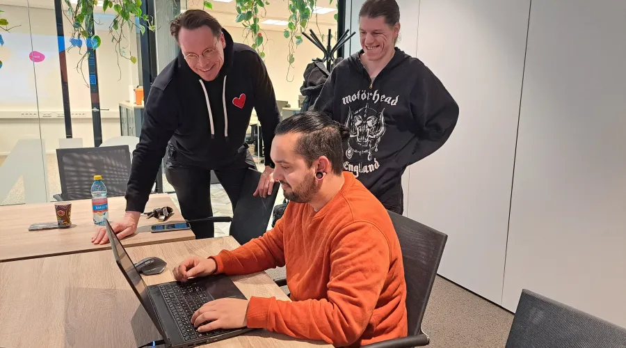Persoon zit achter een laptop en twee collega's kijken met hem mee.