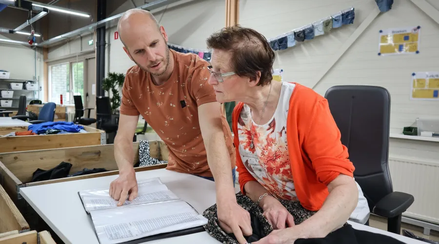 Dame werkt aan tafel en is in gesprek met begeleider